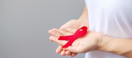 mano sosteniendo la cinta roja para el día mundial del sida de diciembre, el mes de concientización sobre el cáncer de mieloma múltiple y la semana nacional de la cinta roja. concepto de salud y día mundial del cáncer foto