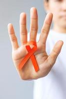 mano sosteniendo cinta naranja para leucemia, día del cáncer de riñón, esclerosis múltiple mundial, crps, mes de concientización sobre autolesiones. cuidado de la salud y el concepto del día del cáncer de palabra foto