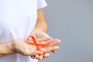 hand holding Orange Ribbon for Leukemia, Kidney cancer day, world Multiple Sclerosis, CRPS, Self Injury Awareness month. Healthcare and word cancer day concept photo