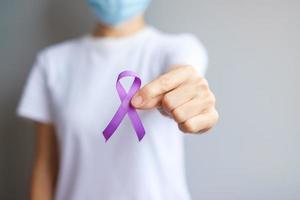 mano que sostiene la cinta morada para el cáncer de páncreas, esófago, testículo, alzheimer mundial, epilepsia, lupus, sarcoidosis, fibromialgia y mes de concientización sobre la violencia doméstica. concepto del día mundial del cáncer foto