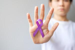 mano que sostiene la cinta morada para el cáncer de páncreas, esófago, testículo, alzheimer mundial, epilepsia, lupus, sarcoidosis, fibromialgia y mes de concientización sobre la violencia doméstica. concepto del día mundial del cáncer foto