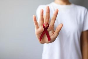 mano que sostiene la cinta roja burdeos para el cáncer de mieloma múltiple de marzo y el mes de concientización sobre el día mundial del sida de diciembre. concepto de salud y día mundial del cáncer foto