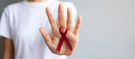 mano que sostiene la cinta roja burdeos para el cáncer de mieloma múltiple de marzo y el mes de concientización sobre el día mundial del sida de diciembre. concepto de salud y día mundial del cáncer foto