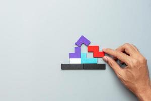 hand connecting Home shape block with colorful wood puzzle pieces on gray background. logical thinking, business logic, solutions, rational, house, real estate and strategy concepts photo