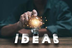 Hands touching light bulbs on the three-dimensional text saying ideas, innovative inspirational new ideas, innovative technologies in science and communication concepts. photo