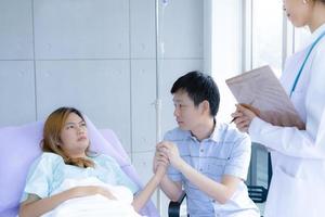 el marido sostiene la mano de una esposa gravemente enferma con un médico en el hospital foto