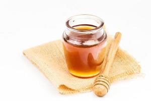 Glass jar full of honey wooden honey dipper on white background photo
