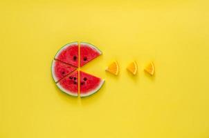 Watermelon eating small slice of orange on yellow background. photo