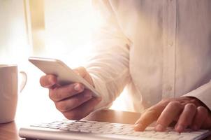 Mans hands using smart phone and computer at office desk. Concept for modern online communications, e-commerce, internet services and apps photo