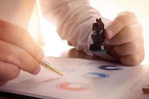 Closeup of businessman working with document graph and holding a chess piece. photo