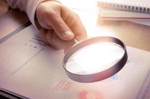 Business analytics and statistics. Businessman study report using a magnifying glass. photo