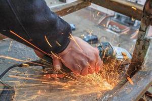 un trabajador corta metal con un molinillo. foto