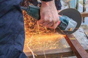 un trabajador corta metal con un molinillo. foto