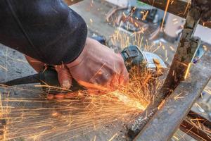 un trabajador corta metal con un molinillo. foto