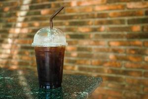 café negro en una taza de plástico transparente sobre una mesa de terrazo de fondo de ladrillo rojo. foto