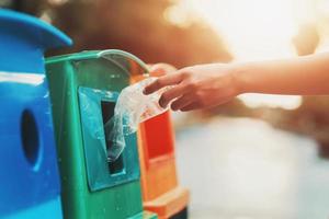 Mano de personas sosteniendo una botella de basura de plástico poniendo en la papelera de reciclaje para limpiar foto