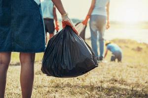 woman hand picking up garbage and hand holding black bag at park photo