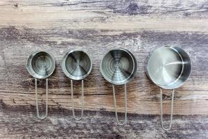 Set of measuring cups made from stainless with a handle on wooden tabletop in top view photo