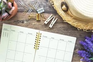 la disposición plana del concepto de verano femenino vintage con un calendario en espiral rosa abierto, sombrero de playa, clips de madera y flores decorativas. foto