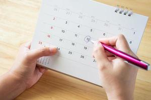 calendar page with female hand holding pen on desk table photo