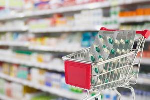 Medical pills capsule in shopping cart with pharmacy drugstore shelves blurred background photo