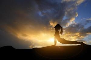 Silhouette young woman practicing yoga on the mountain at sunset. Meditation or exercise concept. photo