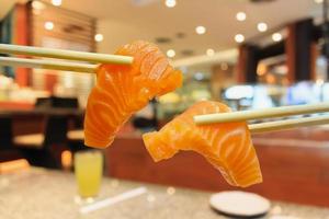 salmon sashimi in chopsticks with japanese restaurant interior photo