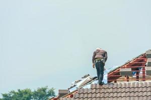 techador de construcción instalando tejas en el sitio de construcción de viviendas foto