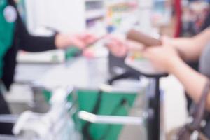difuminar la mano de una clienta dando tarjeta de crédito al cajero en el fondo desenfocado de la caja del supermercado foto