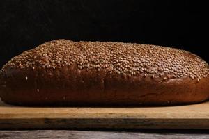Bun lies on cutting board sprinkled with sesame seeds on dark background. photo
