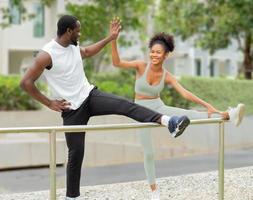 Young African American family happy stretching after jogging outdoor in the park. Cheerful couple clap their hands high five after exercising achievement. Husband and wife together healthy concept. photo
