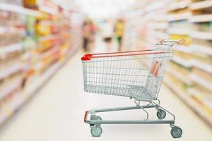 Supermarket aisle blur defocused background with empty red shopping cart photo