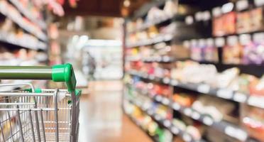 Empty green supermarket shopping cart with abstract blur grocery store aisle defocused background photo