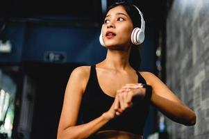 girl in the gym exercising Listening to music with white over-ear headphones and using a digital heartbeat timer. systematic exercise Exercises are structured. photo