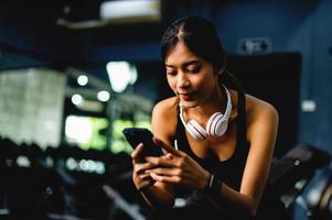 una chica en el gimnasio haciendo ejercicio usa un teléfono celular escuchando música con auriculares blancos y usando un temporizador digital de latidos del corazón. Los ejercicios de ejercicios sistemáticos están estructurados. foto