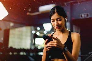 Asian woman in the gym and playing on the phone while listening to music before exercising in the fitness center photo