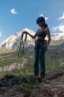 A woman in a helmet coils a rope against the background of a large mountain photo