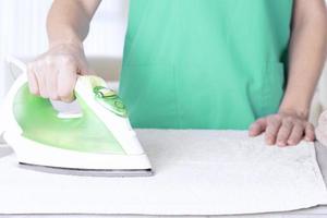 Caucasian woman, wife, mother, housewife, housekeeper, maid ironing linen with electric iron on ironing board. Home interior background. soft focus. photo