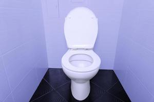 A white toilet bowl with an open lid on a black tiled floor and purple walls. photo