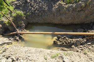 Old rusty metal pipes in a pit with water, water supply system in a mountainous area. Breakthrough of a rusty pipeline. photo