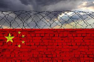 The flag of the country of China, on a wall of bricks with barbed wire, against a backdrop of a stormy sky. photo