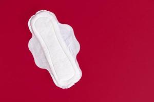 One Feminine Sanitary Pad, Napkin. Means of feminine hygiene during the menstrual cycle. Red background. Copy space. photo