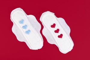 Three blue and red hearts as a symbol of transgender, menstrual cycle on a feminine sanitary napkin. Feminine hygiene products during the menstrual cycle. Red background. Copy space. photo