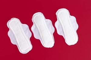 Three feminine sanitary pads, napkins. Feminine hygiene products during the menstrual cycle. Red background. Copy space. photo