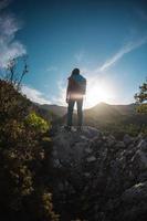 The silhouette of a woman with a backpack against the backdrop of a mountain at sunset photo