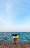 una niña junto al mar con una bandera ucraniana foto