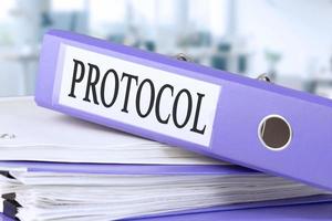 Protocol, text written in a folder with documents in trendy purple color, lying on a stack of papers, documents on an office table, against a background of soft blur office background. photo