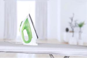 electric iron stands on an ironing board against the backdrop of a home interior. Blurred background, soft focus. photo