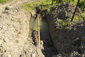 Old rusty metal pipes in a pit with water, water supply system in a mountainous area. Breakthrough of a rusty pipeline. photo