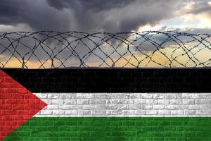 A brick wall with barbed wire in the colors of the national flag of Palestine against a stormy sky. Crisis and hybrid war, border closures. photo